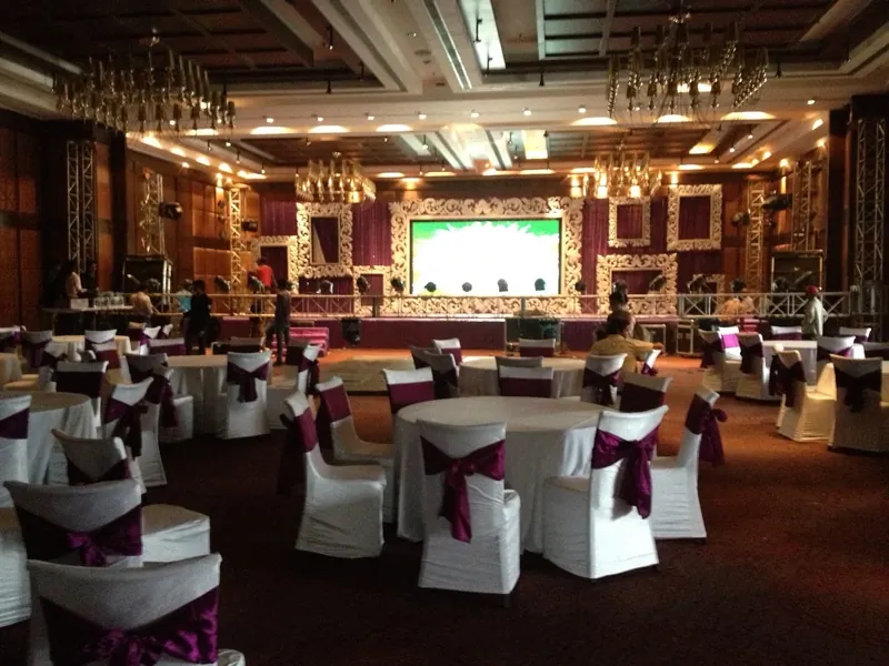 A hall set for a corporate event, round tables in plum sashes facing an ornate white stage and LED wall