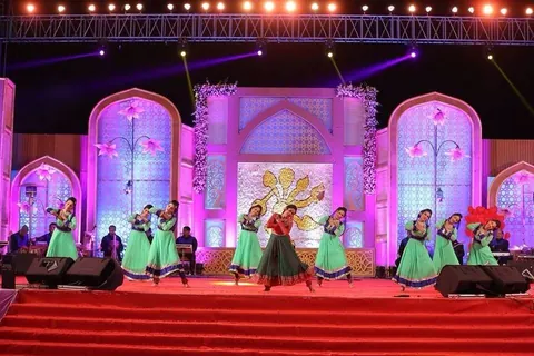 Dancers in matching green costumes holding the same pose mid-routine on a lit stage, musicians seated at either side