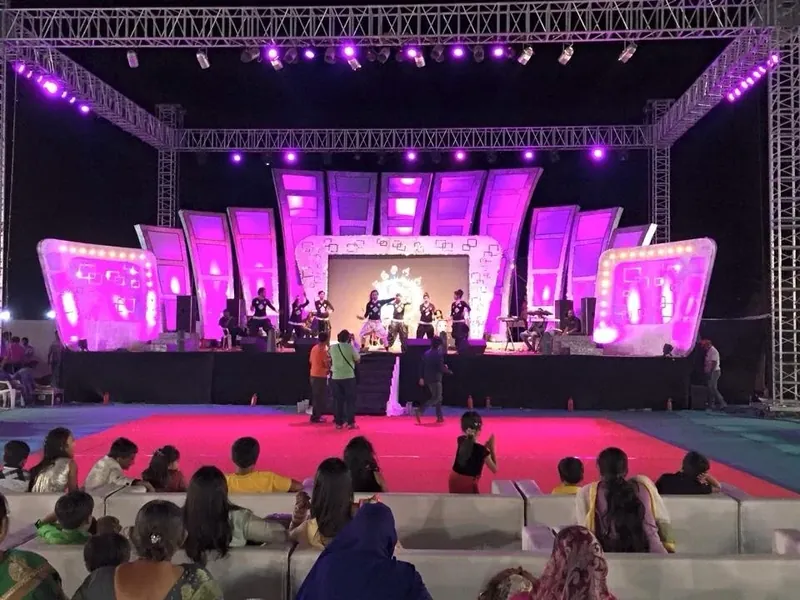 A large outdoor stage under truss lighting washed in magenta, with an audience watching